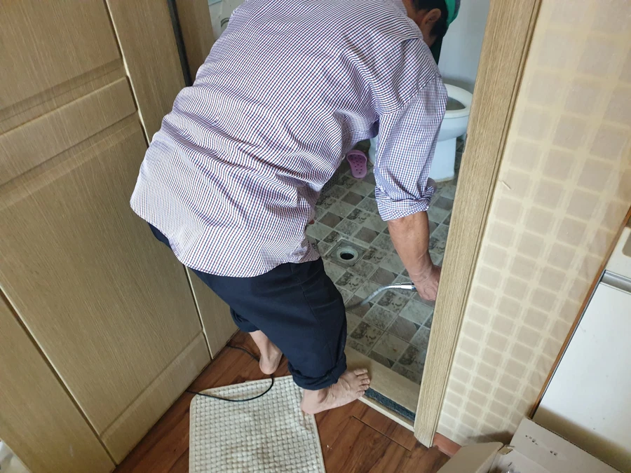변기 점검 참고 사진, 바닥 배수구를 도구로 점검하는 모습
