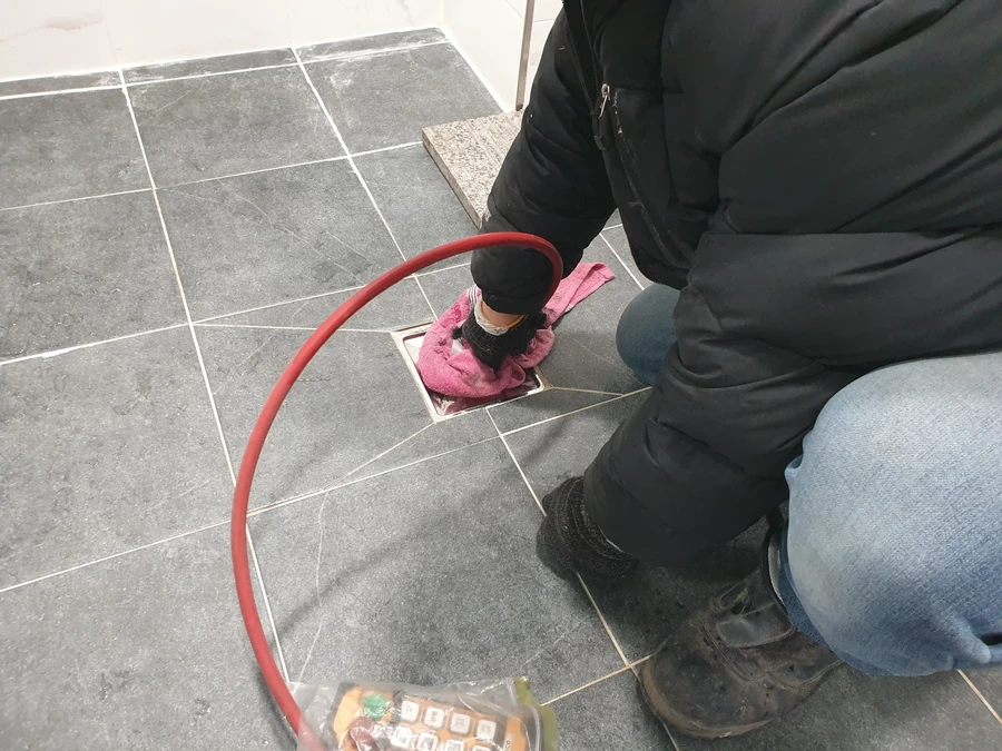 붉은 호스와 분홍 천으로 화장실 바닥을 닦는 작업자