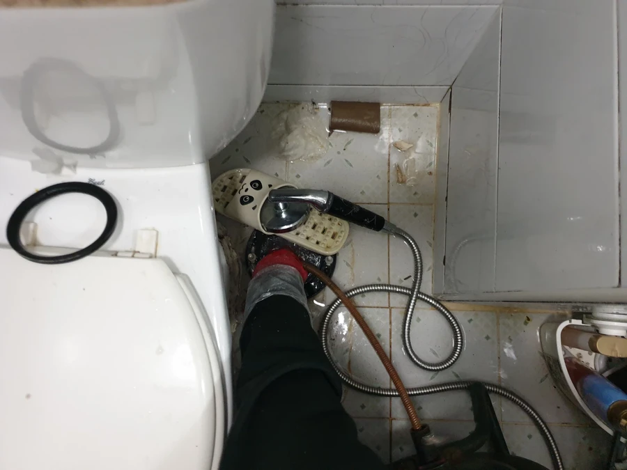 바닥 근처에서 스네이크 케이블 선단부를 다루는 모습, 배경에 변기가 보임