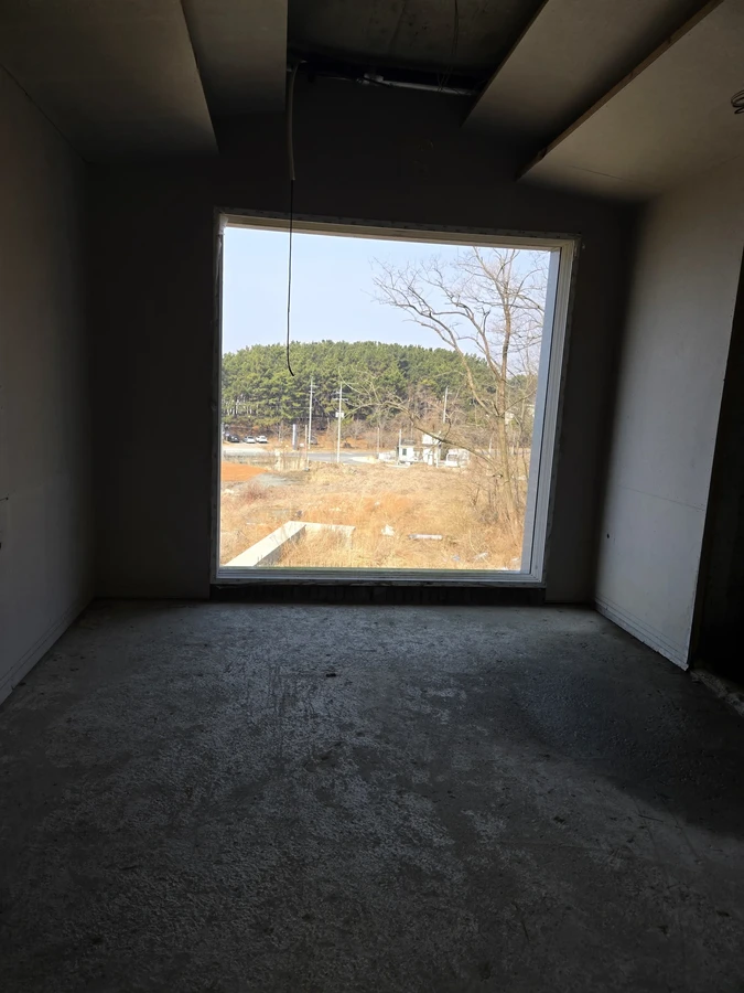 어두운 실내의 큰 창 너머로 들판과 나무가 보이는 모습
