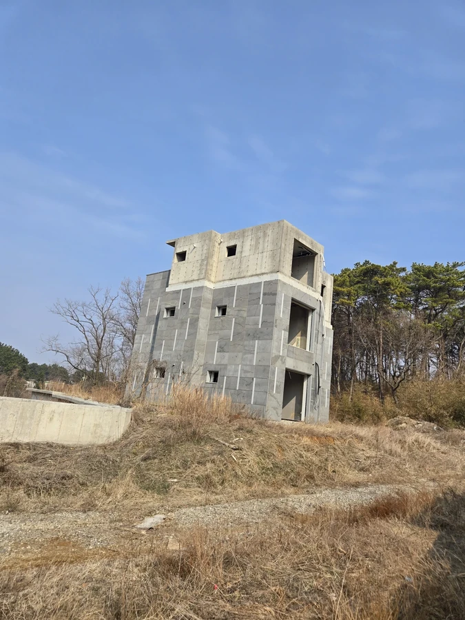 마른 풀 부지 위에 서 있는 3층 규모의 콘크리트 구조물 외관