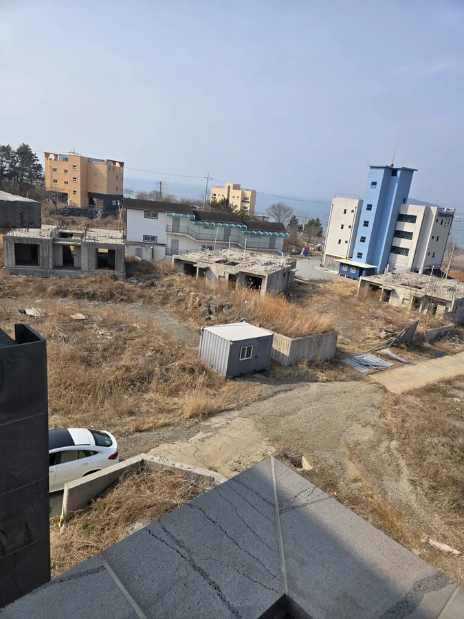 높은 곳에서 내려다본 마른 풀 부지와 주변 건물, 컨테이너가 보이는 현장 전경